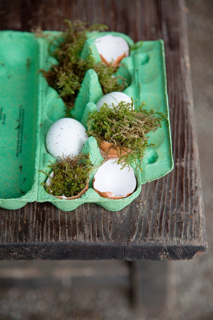 Easter arrangement of green egg box, moss and egg shells on wooden table