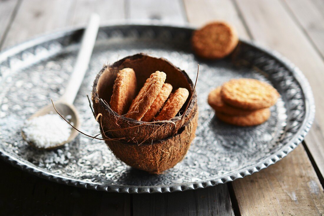 Coconut biscuits in a coconut husk on a tray with a spoon of desiccated coconut