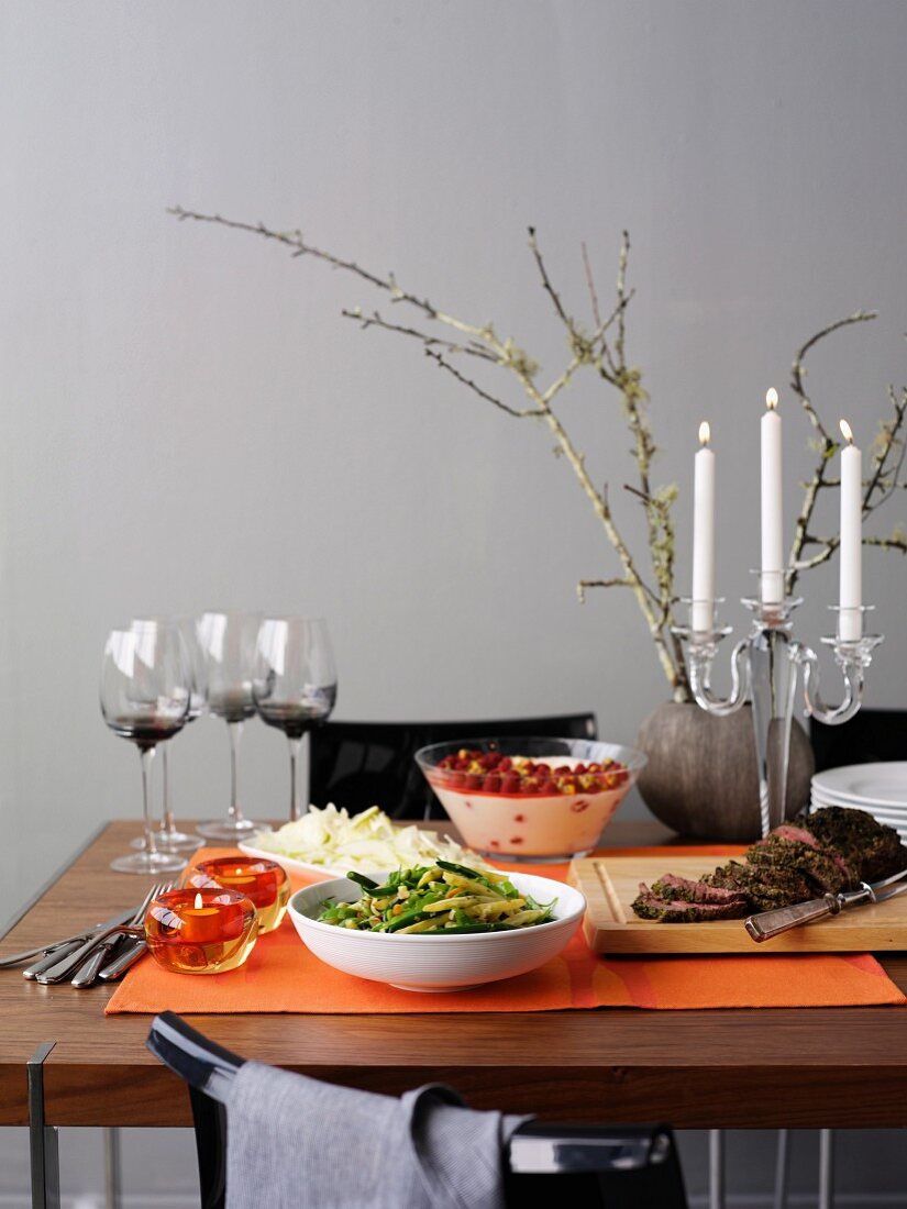 Gedeckter Tisch mit gemischten Bohnen, Rinderfilet, Salat, Dessert, Wein und Kerzen