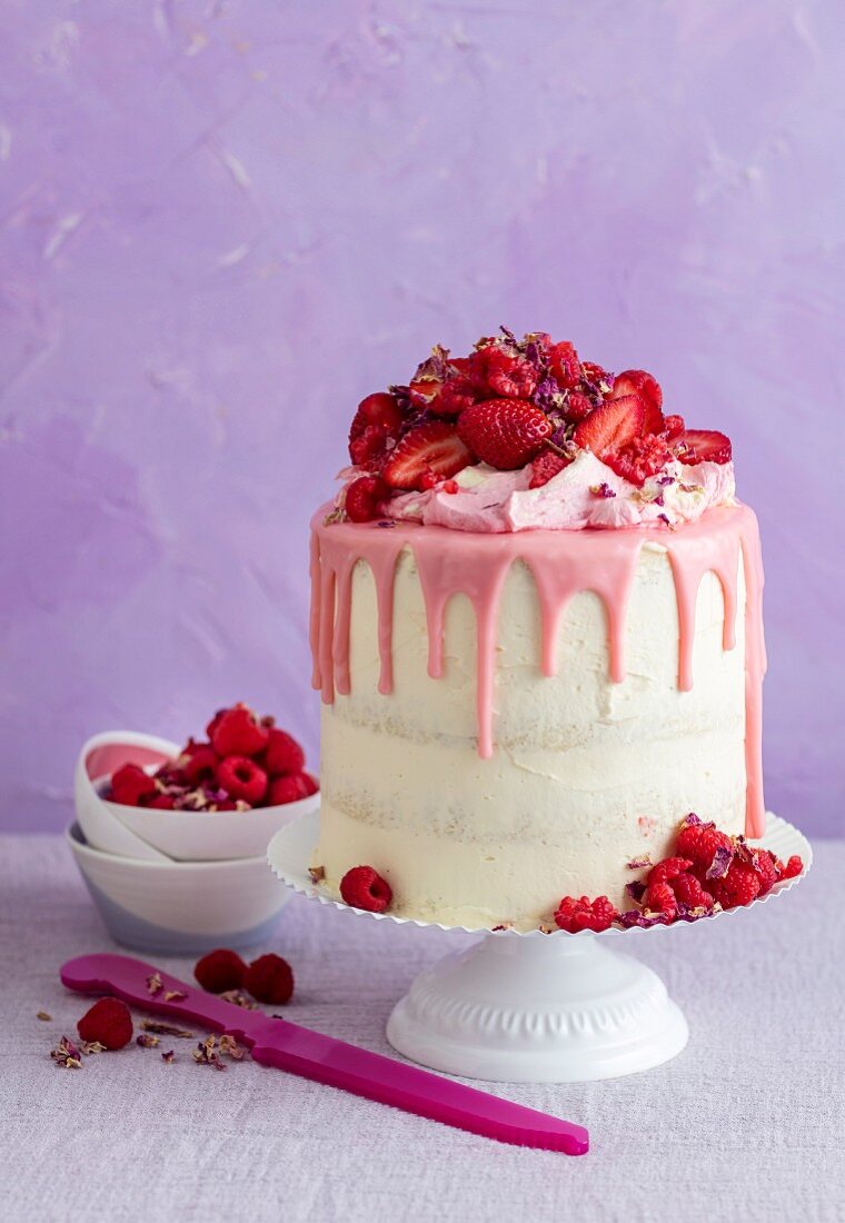 Kuchen mit heller Buttercreme, rosafarbener Ganache, Himbeeren, Erdbeeren und Rosenblättern
