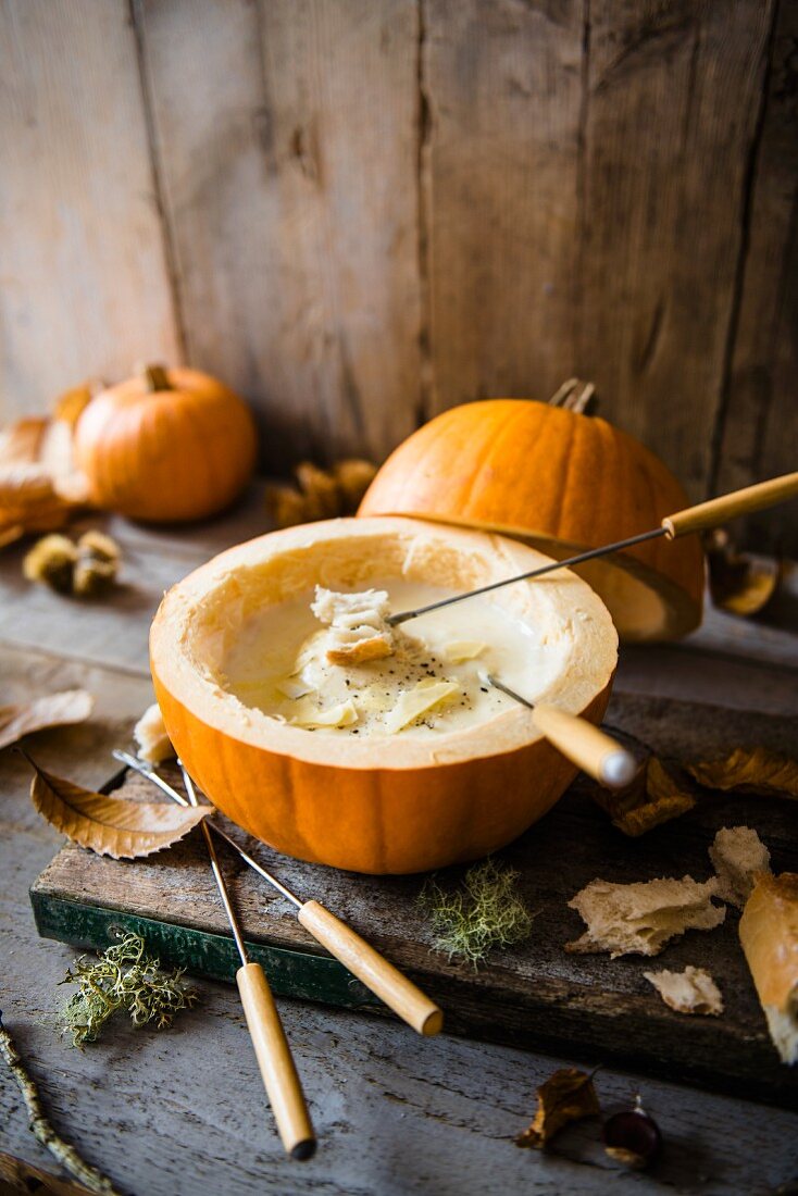 Cheese fondue served inside a hollow pumpkin with bread and autumnal leaves
