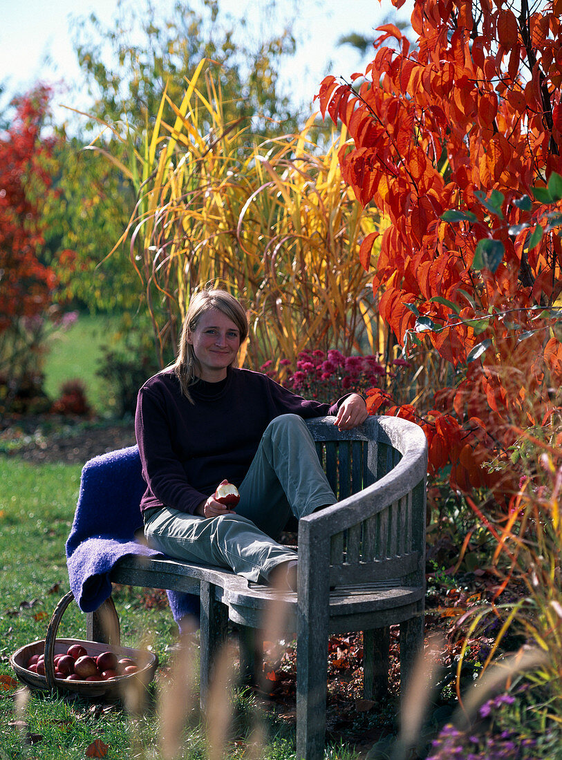 Junge Frau auf Bank am Herbstbeet