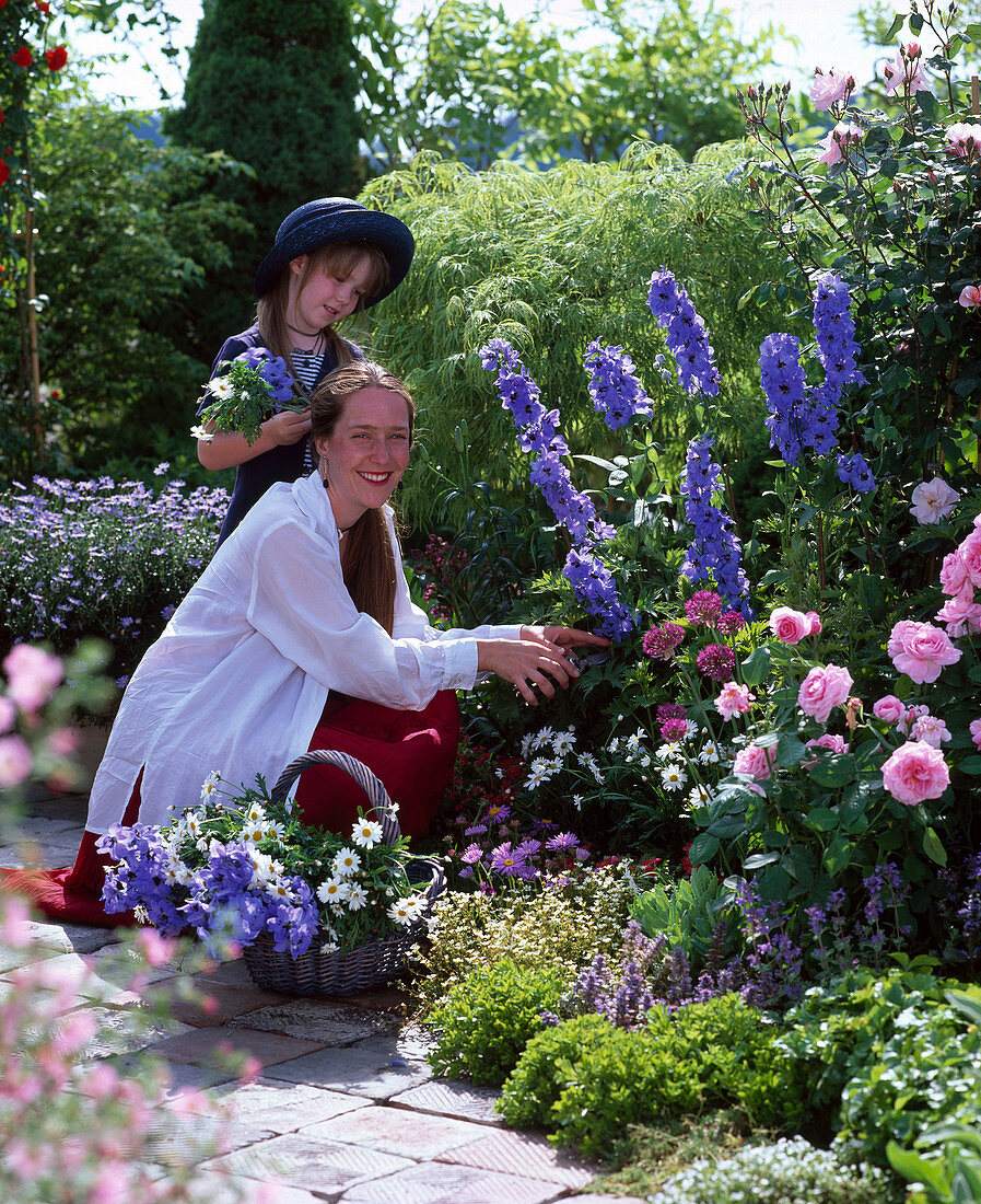 Mother and daughter with hat cutting flowers for bouquet