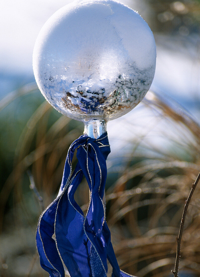 Silver garden ball on stick with blue ribbon and hoarfrost