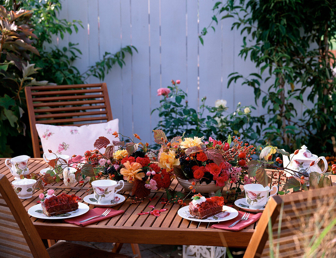 Tischdeko mit Gesteck von Rosenblüten, Rosa (Hagebutten), Viburnum (Schneeballbeeren)