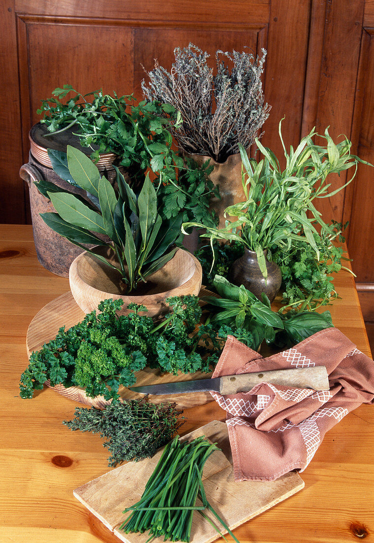 Various herbs with knife and cutting board on wooden table