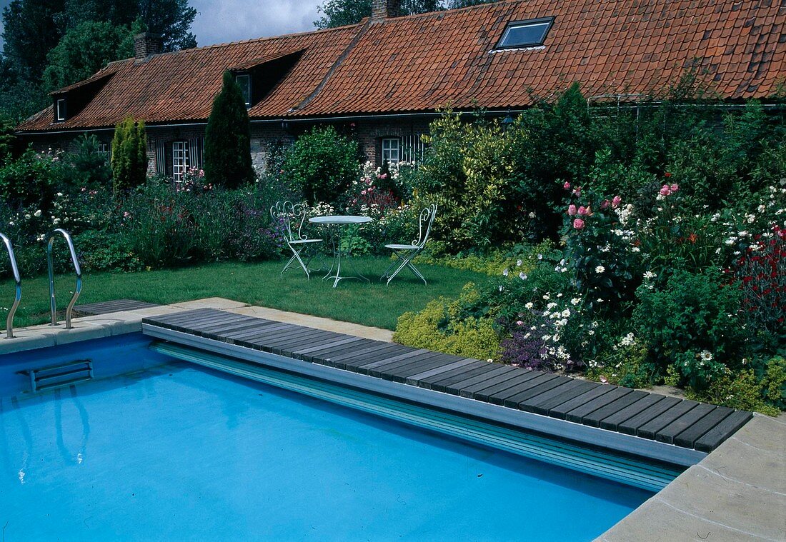 Swimmingpool, kleine Sitzgruppe auf dem Rasen, Beet mit Rosa (Rosen), Alchemilla (Frauenmantel), Leucanthemum (Margeriten), Nepeta (Katzenminze) und Sträuchern