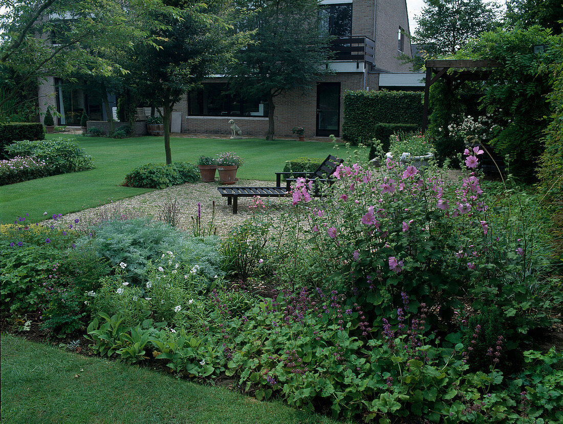 Kiesterrasse mit Liege und Terrassenbeet: Lavatera (Strauchmalve), Salvia verticillata 'Purple Rain' (Rauhblättriger Salbei), Geranium (Storchschnabel)