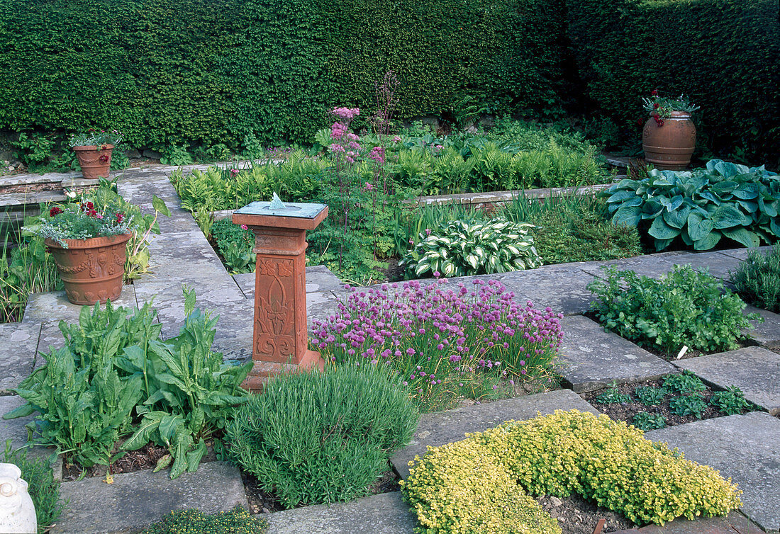 Mit Beton-Platten abgeteilte Beete, Sonnenuhr und bepflanzte Töpfe aus Terrakotta