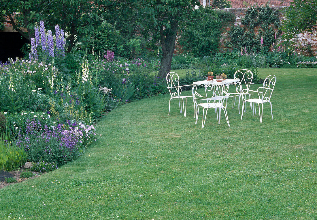 Early summer perennial bed with Delphinium (delphinium), Digitalis (foxglove), Iris (iris), Salvia (sage), white seating area on the lawn