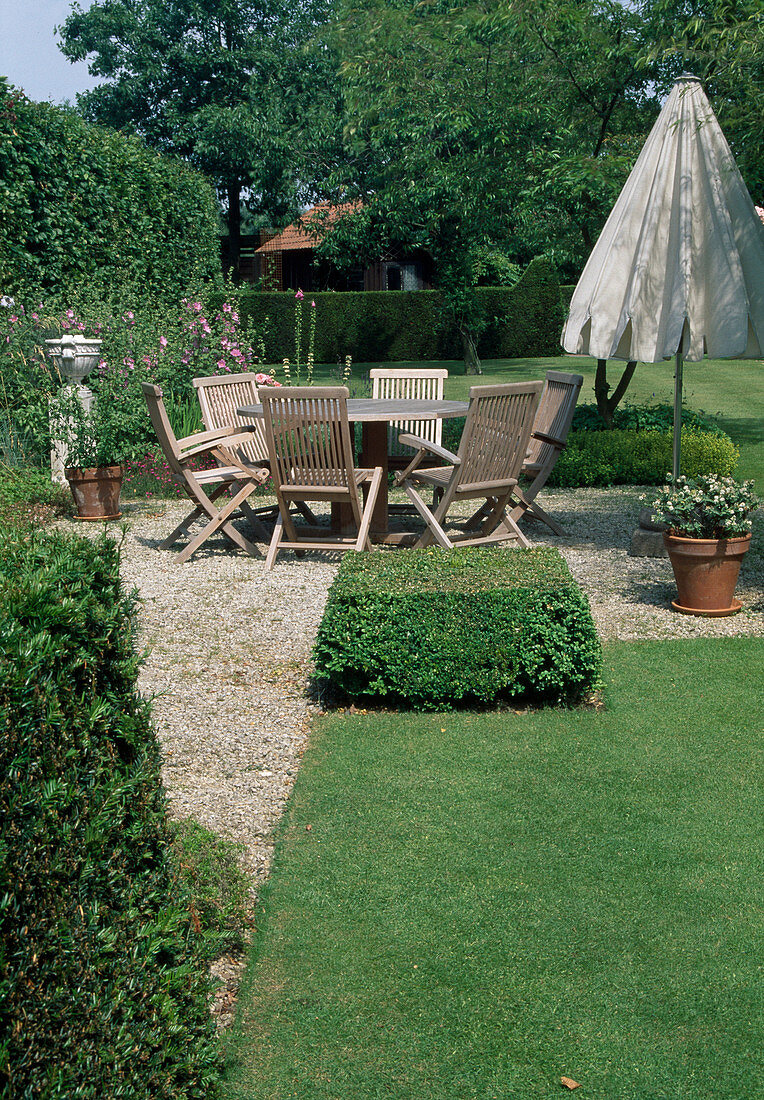 Wooden seating group on gravel terrace, Buxus (boxwood) cut into squares