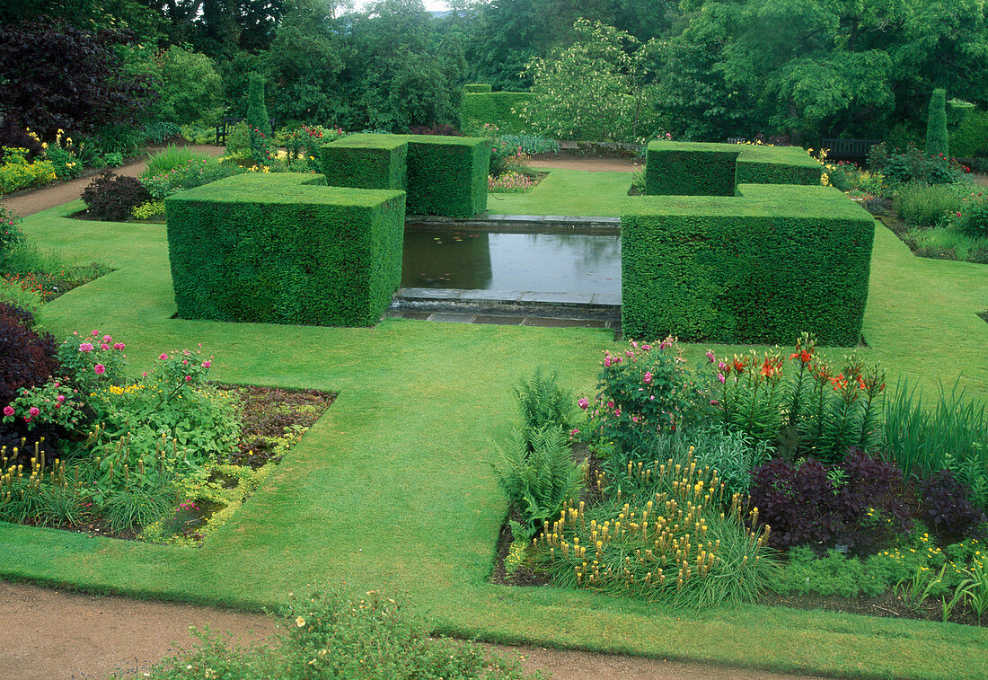 Formal garden with strictly trimmed hedge elements around water basins, lawn paths, perennial beds