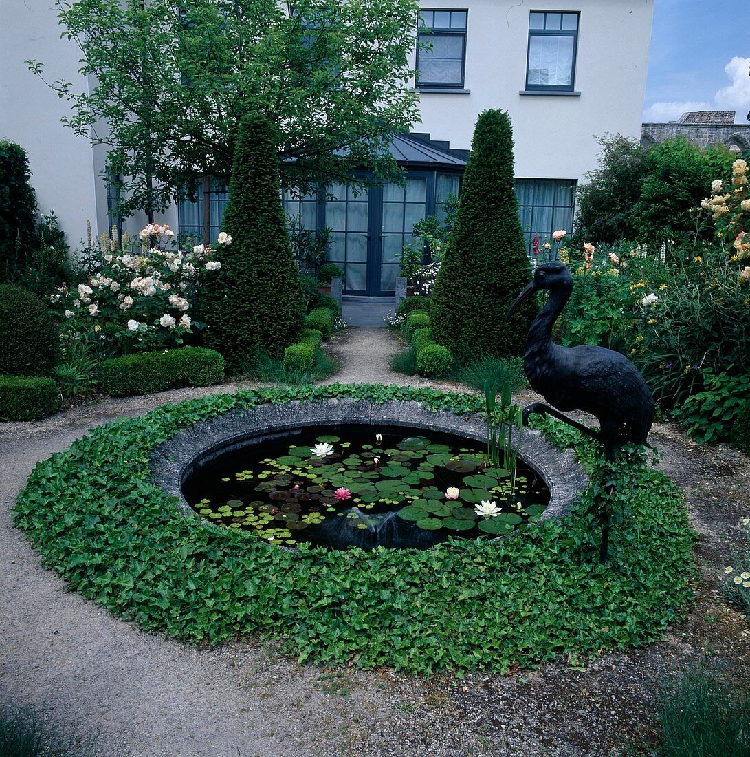 Round water basin with water lilies and ivy as border in garden in front of house