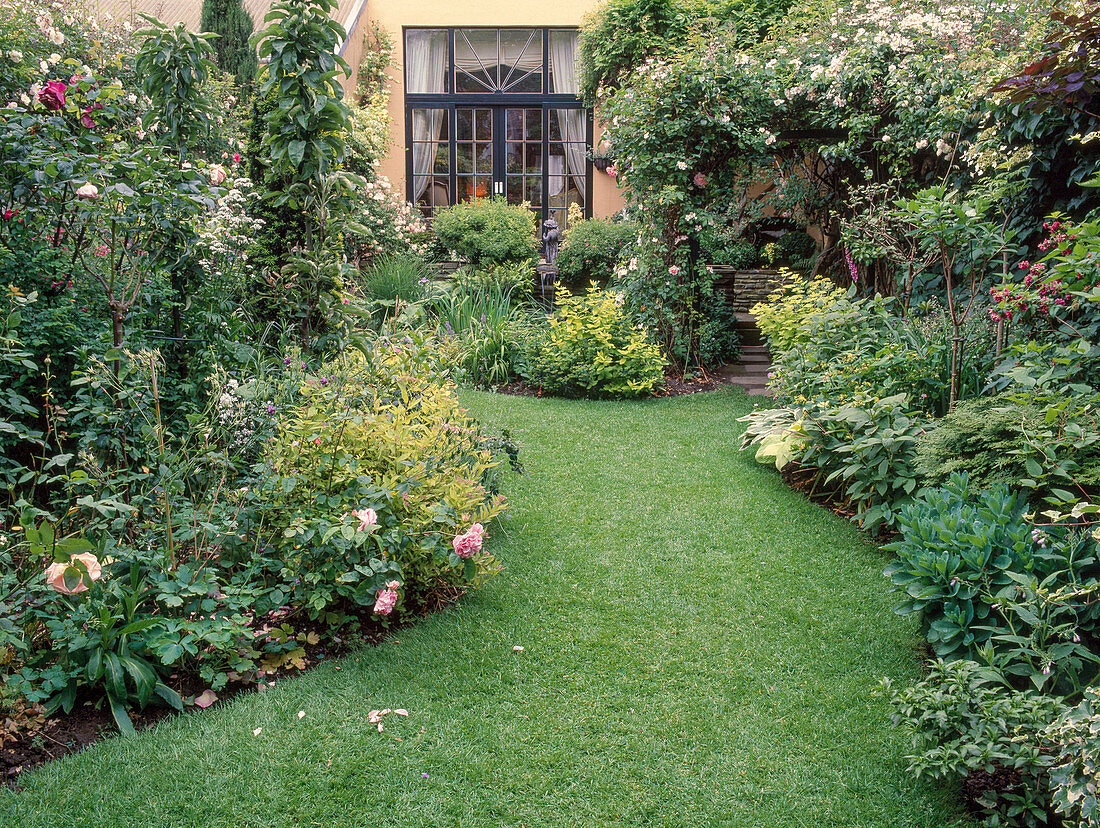 Kleiner Garten mit Rosa 'Francis E. Lester' (Ramblerrose), Kletterrose, Spiraea (Spierstrauch), Hosta (Funkie), Sedum (Fetthenne), Rasenweg zwischen Beeten