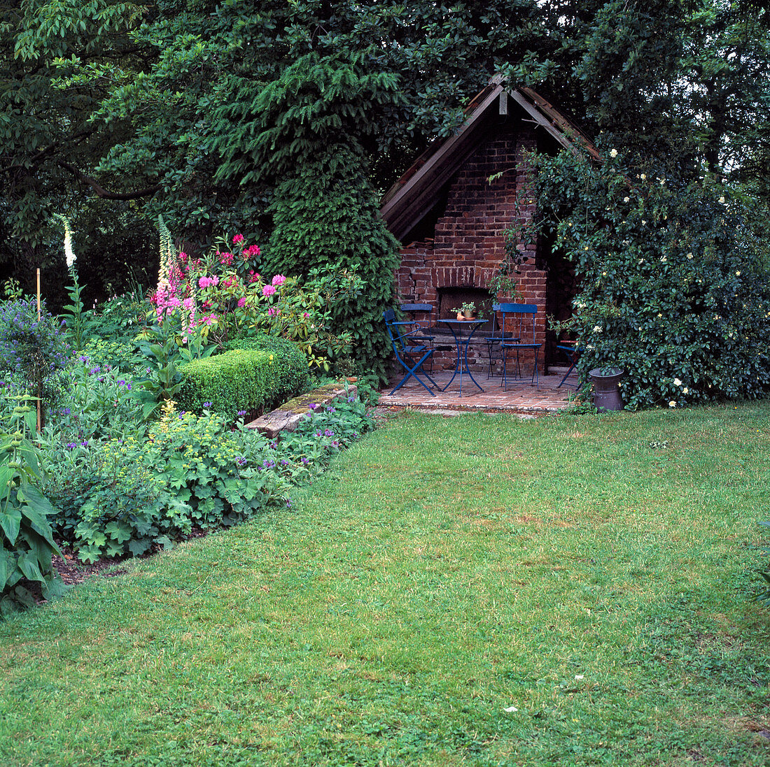 Gartenhaus mit Backofen und blauer Sitzgruppe, im Beet Alchemilla (Frauenmantel), Digitalis (Fingerhut), Centaurea (Flockenblume)