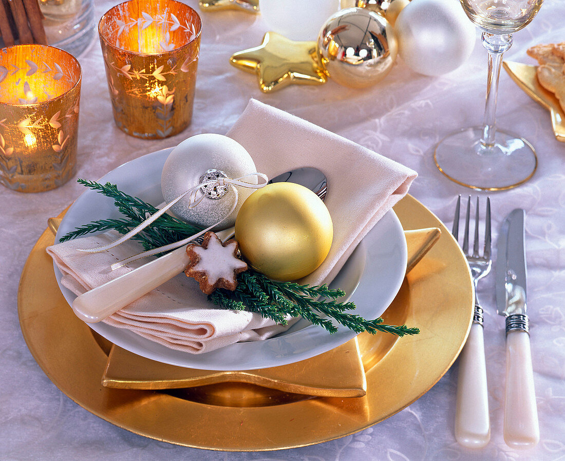 Tellerdekoration mit goldenen Platzteller, weißer Serviette und Christbaumschmuck