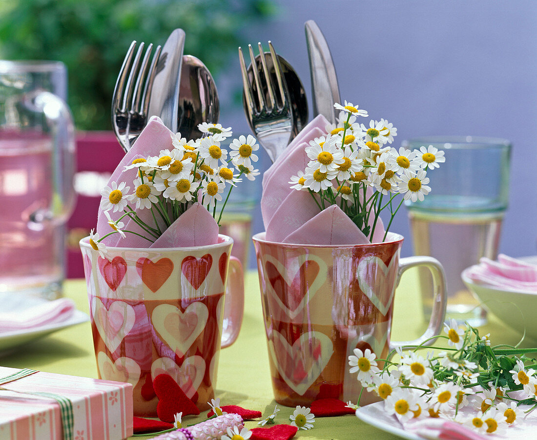 Cups with Matricaria (= Chamomilla, camomile), cutlery, pink napkins