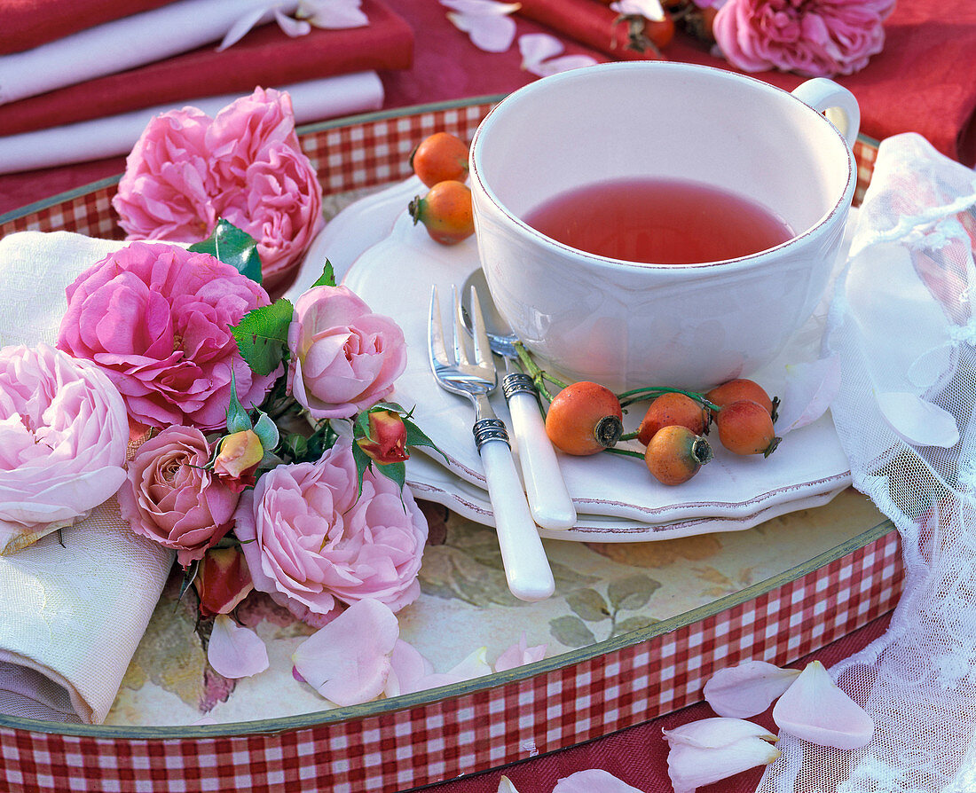 Gebinde von rosa Rosa (Rosen, Hagebutten) an gerollter Serviette, Teetasse