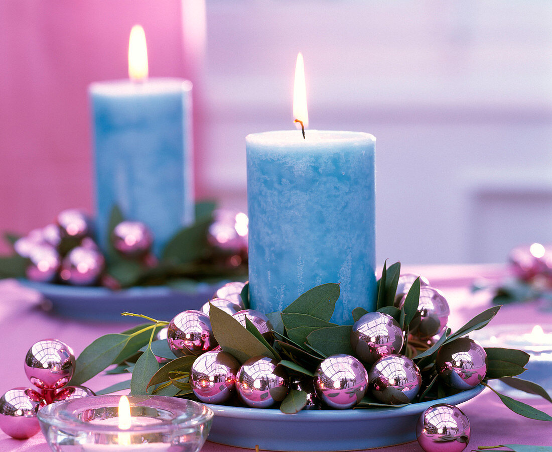Wreath made of eucalyptus, pink Christmas tree balls around blue candle on