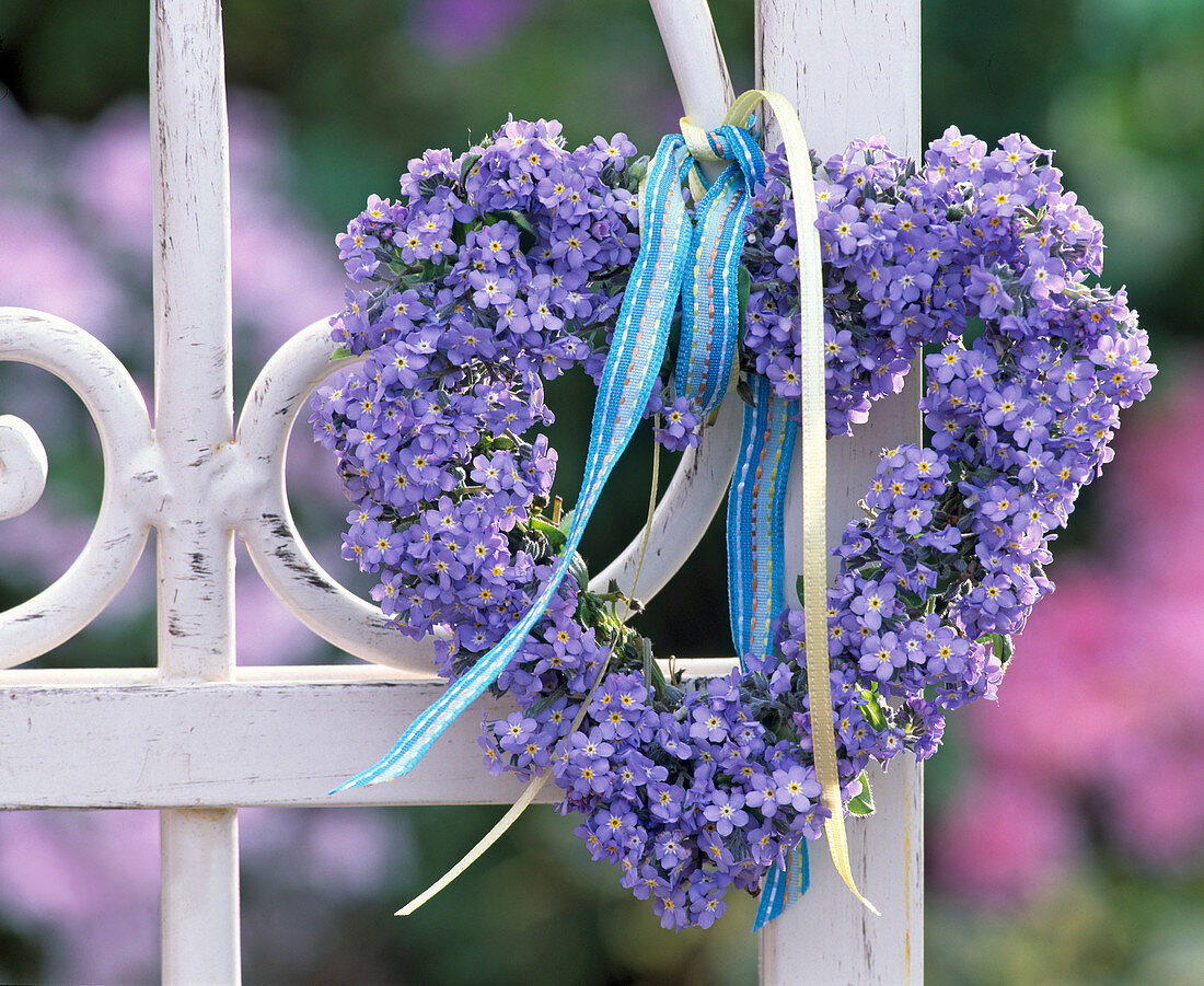 Heart shaped wreath of myosotis on white metal fence