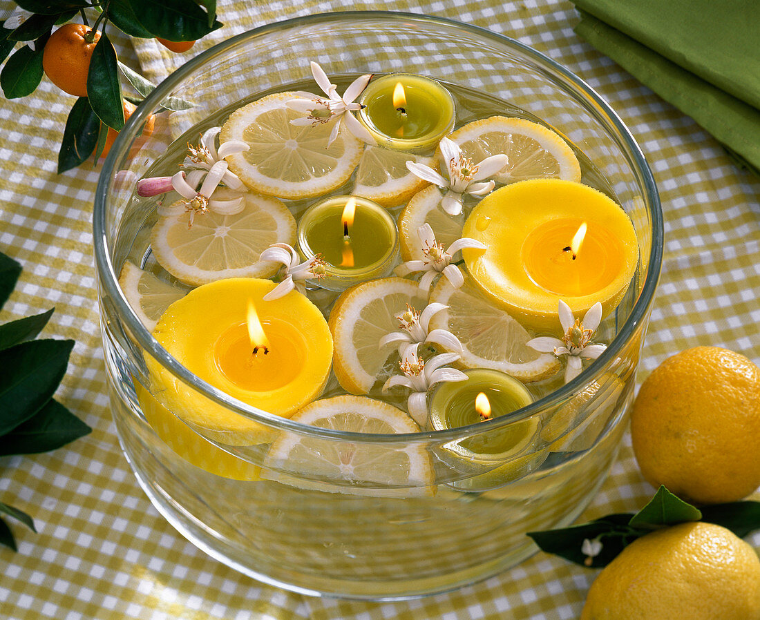 Blüten und Scheiben von Citrus limon (Zitronen), Schwimmkerzen in Glasschale