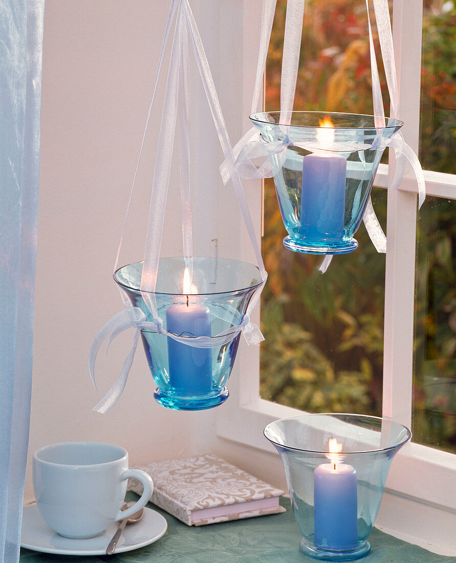 Glasses with blue pillar candles hanging in the window, cup, book
