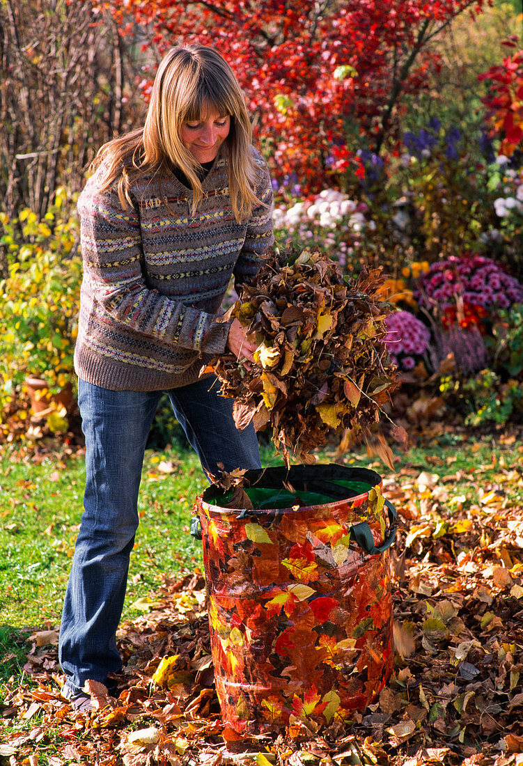 Young woman filling leaves into garden waste bag