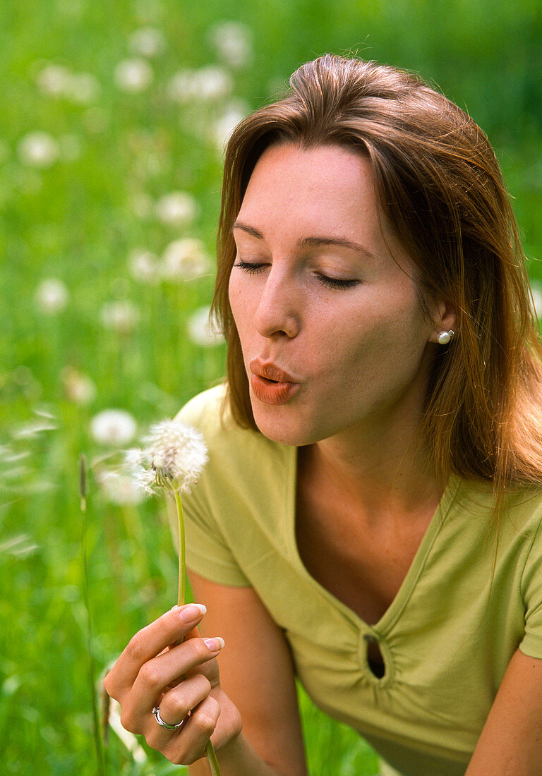 Woman blowing Taraxacum (dandelion) seed head