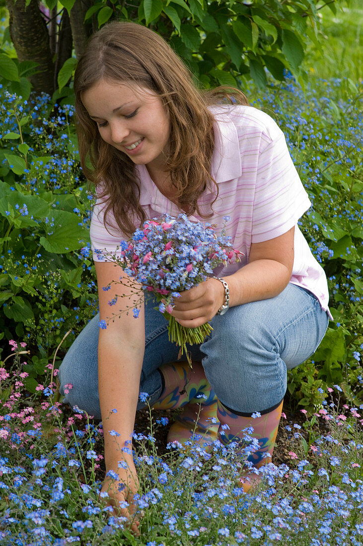 Woman picking bouquet of myosotis (forget-me-not) and dicentra