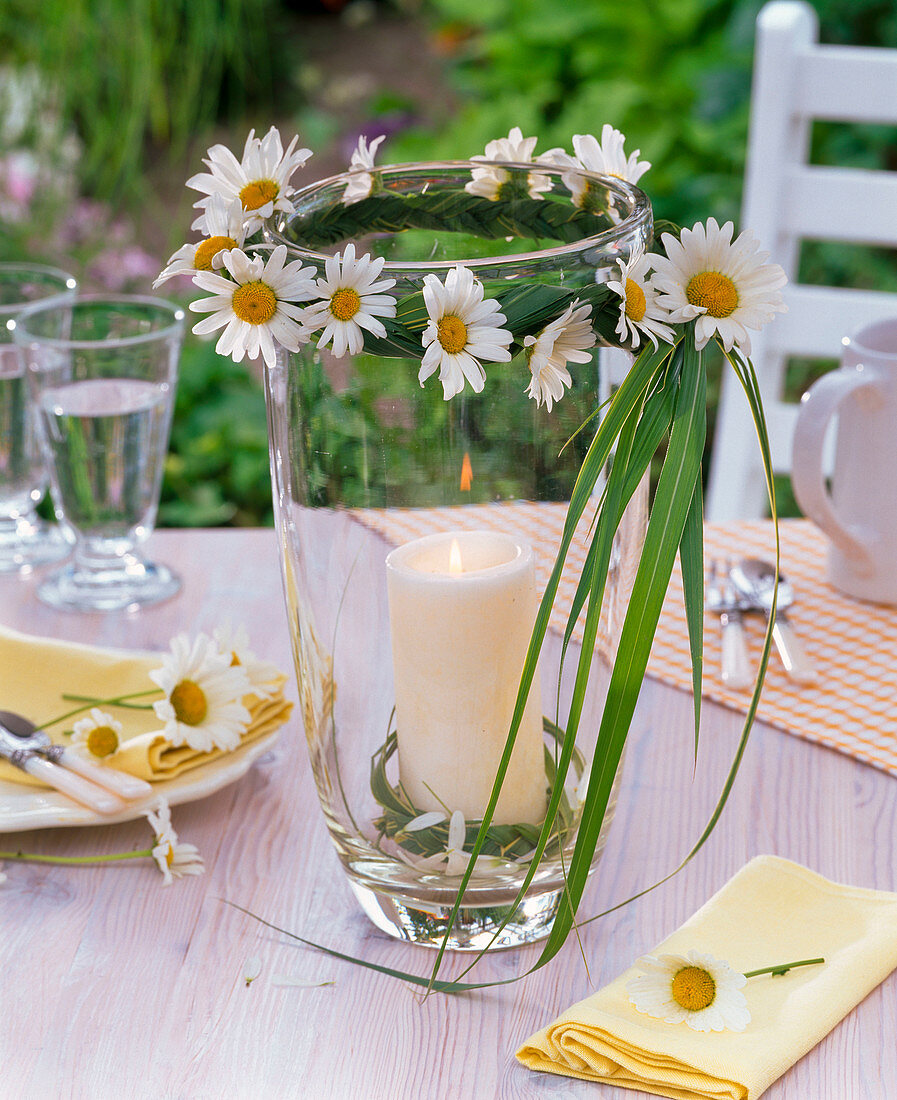 Lantern with leucanthemum and grasses around tall glass