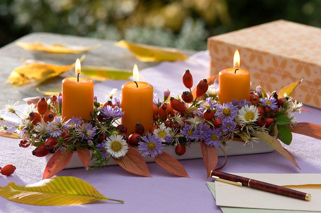 Autumn arrangement with candles, asters and rose hips