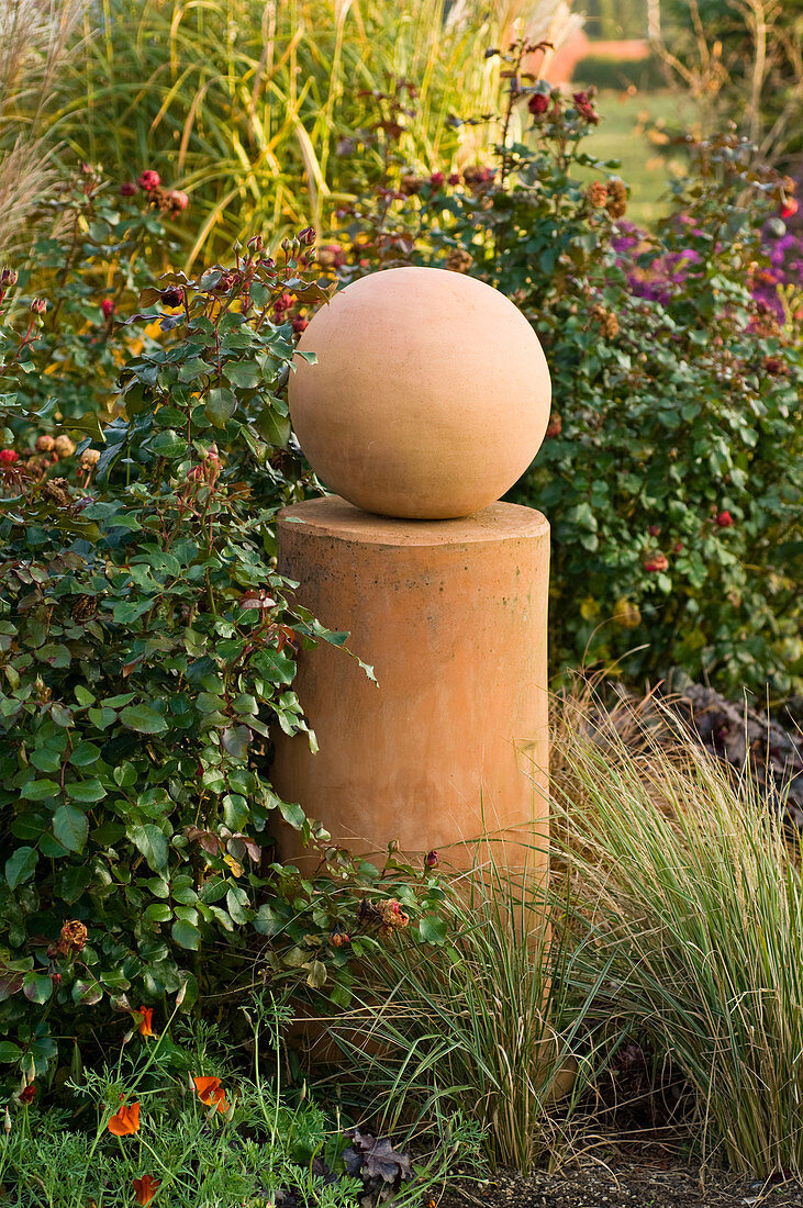 Terracotta column with ball as decoration between Rosa (roses)