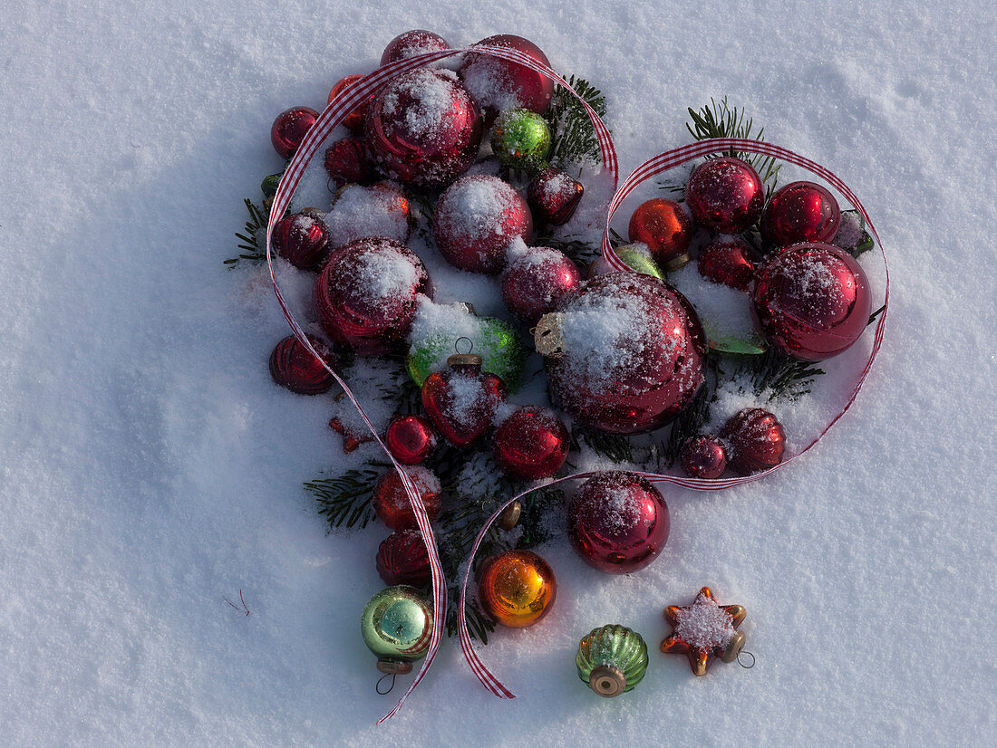 Heart made of Christmas tree ornaments laid in snow