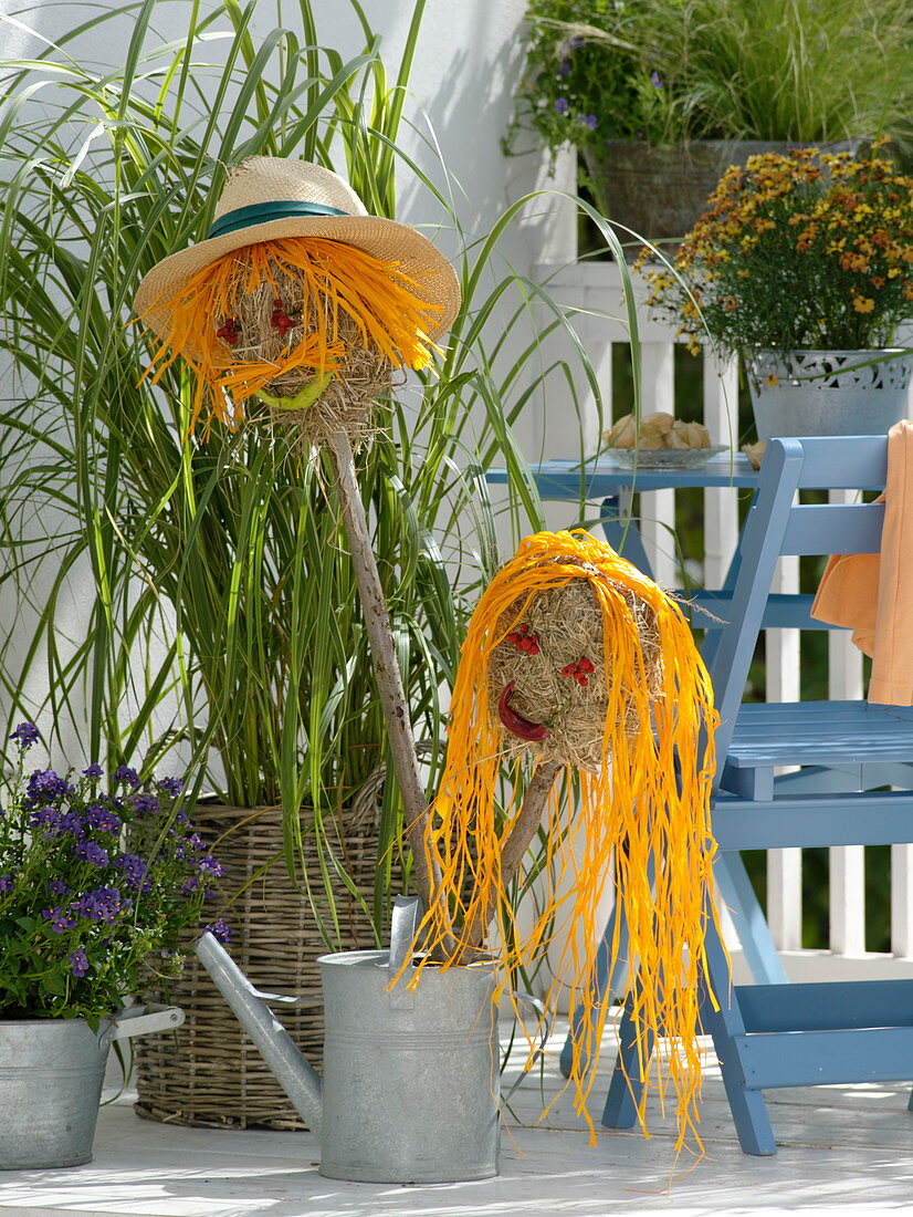 Köpfe aus Heu mit Haaren aus gelbem Bast in Gießkanne gestellt