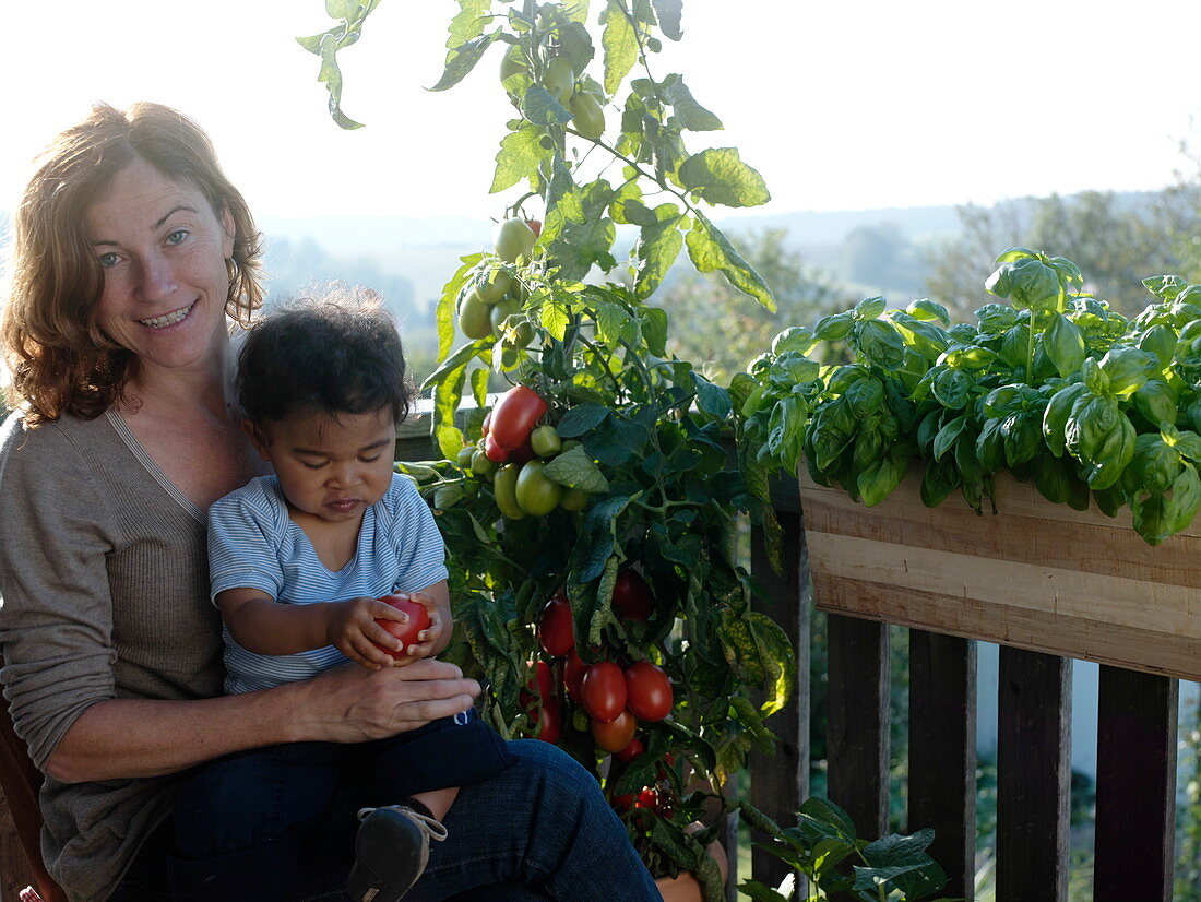 Kleiner Junge mit Tomate auf Mamas Schoß