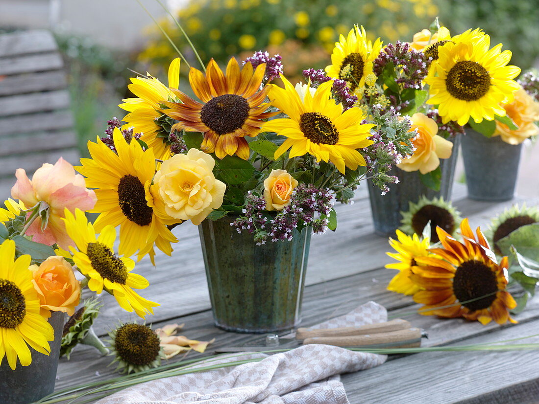 Bouquets in tin vases with sunflowers and roses on a wooden table