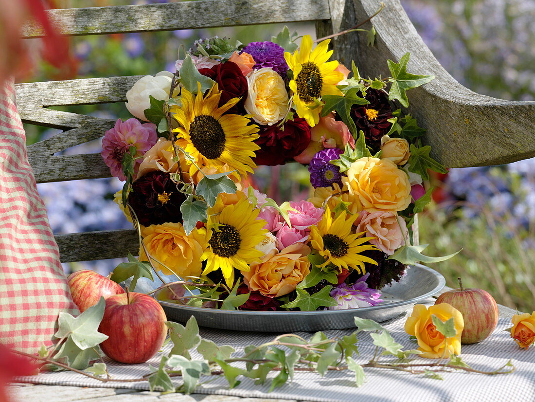 Wreath of sunflowers, roses and dahlias on a wine box leaning against a bench