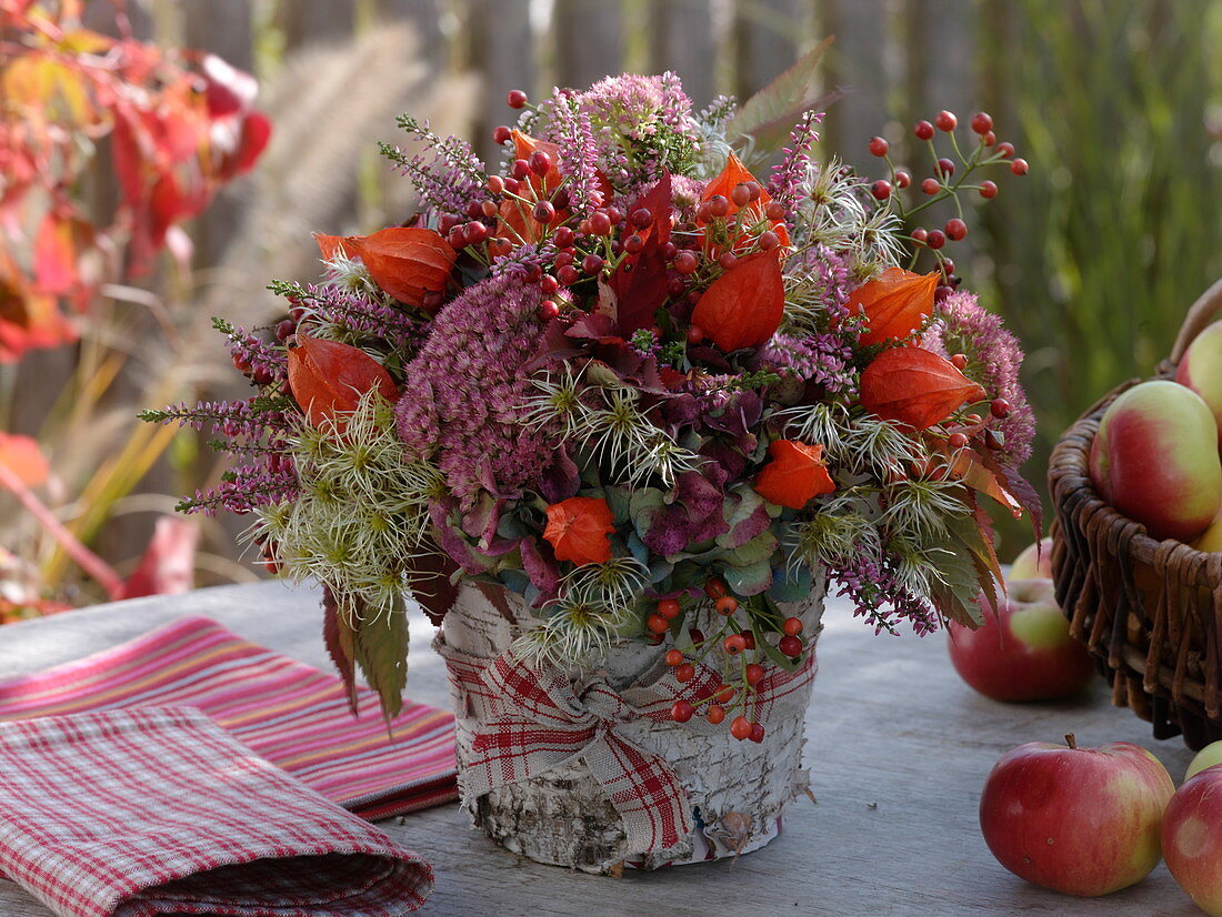 Autumn bouquet with stonecrop, lampion flower and rose hips in a birch pot