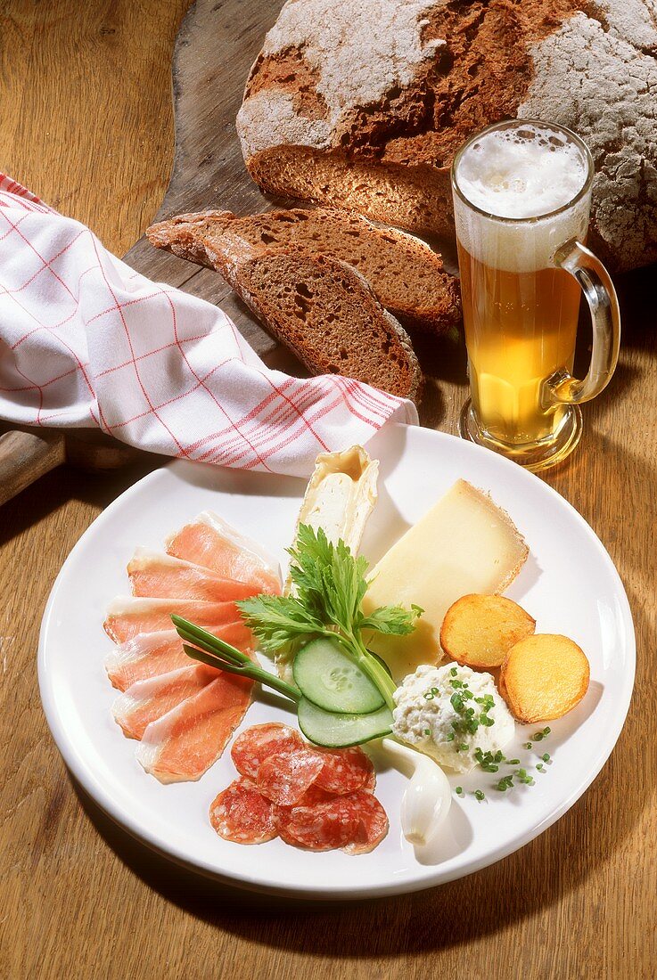Mixed Appetizer Plate with Ham, Salami, Cheese, and Vegetables with dark Bread and Glass of Beer