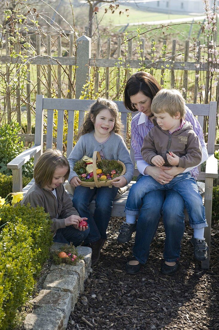 Frau mit Kindern im Garten auf der Bank, Spankorb als Osternest
