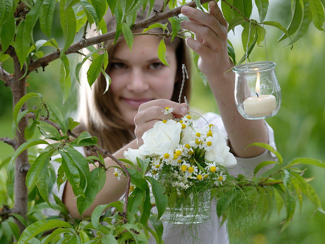 White bouquet of herbs in a glass and small lanterns hung on a tree (1/2)