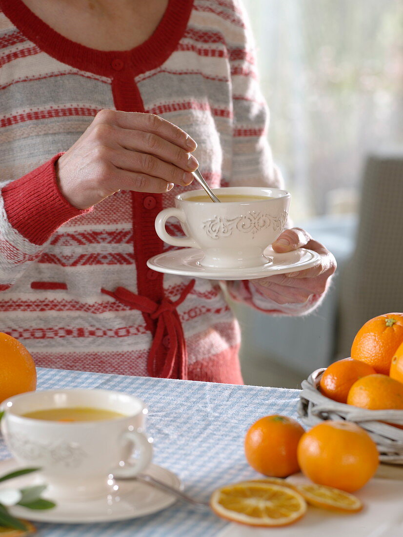 Woman with hot orange tea in cup, oranges