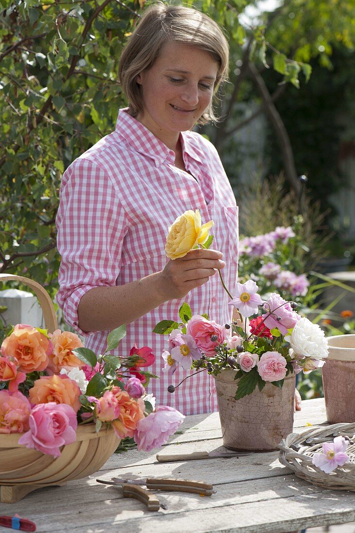 Frau steckt kleinen Strauß mit gemischten Rosa (Rosen) und Anemone