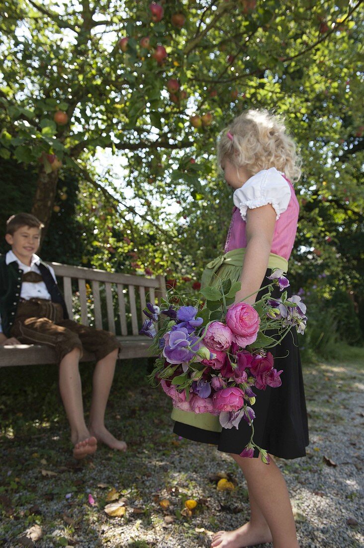 Mädchen im Dirndl mit Duftstrauß aus Rosa (Rosen) und Lathyrus odoratus