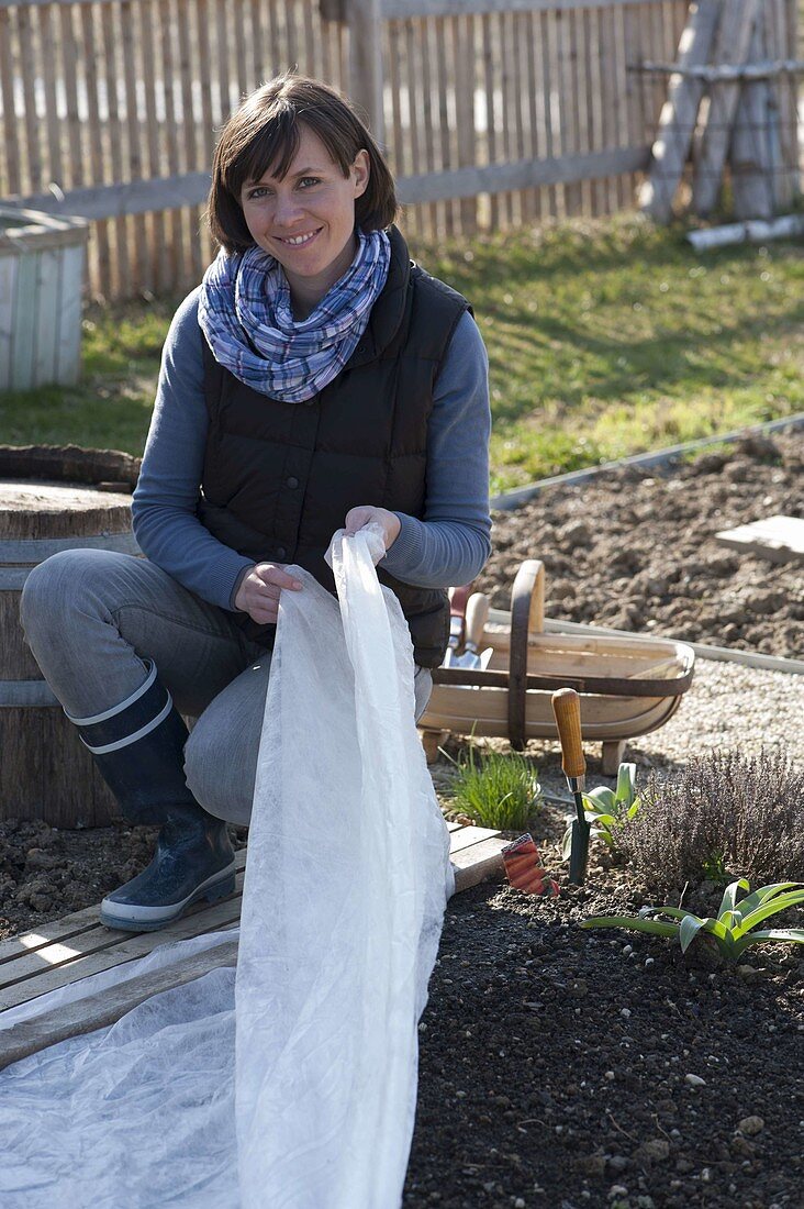 Frau deckt Beet mit ausgesäten Gemüse-Samen mit Vlies ab
