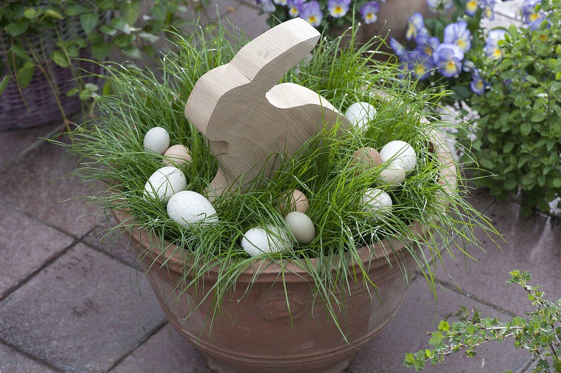 Topf mit Gras als Osternest mit Holz-Osterhase und Ostereiern