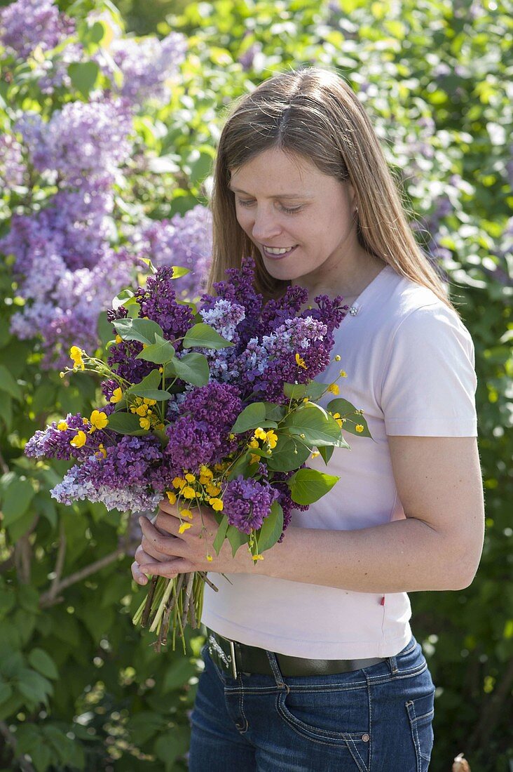 Woman with fragrant bouquet of Syringa (lilac) and Ranunculus acris