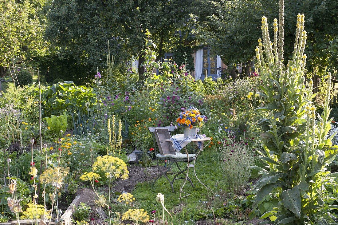 Kleiner Sitzplatz zwischen Beeten mit Stauden und Sommerblumen