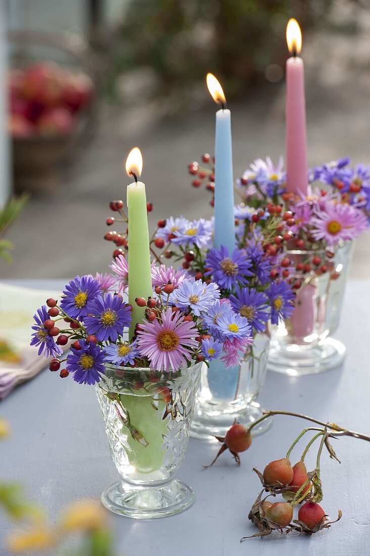 Kerzengläser mit Aster (Herbstastern) und Rosa (Hagebutten) in Reihe