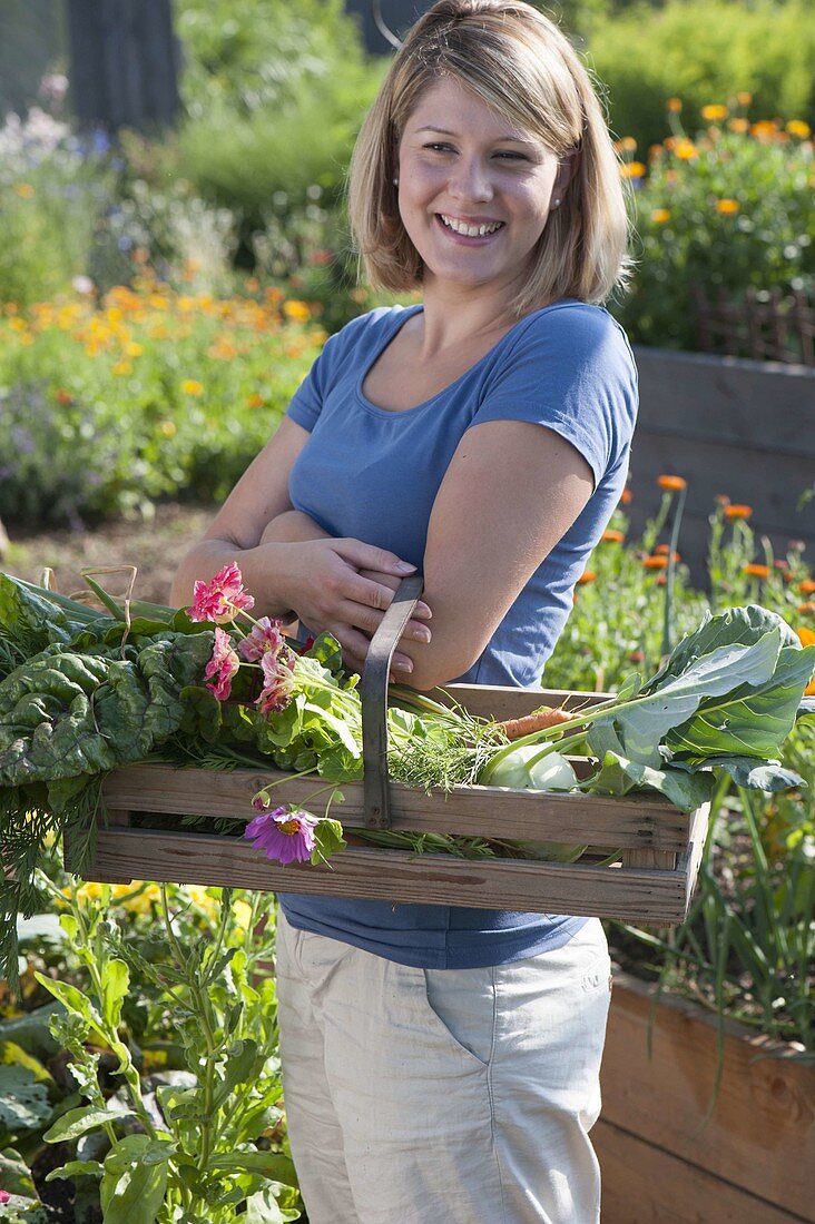 Woman with freshly harvested vegetables between raised beds